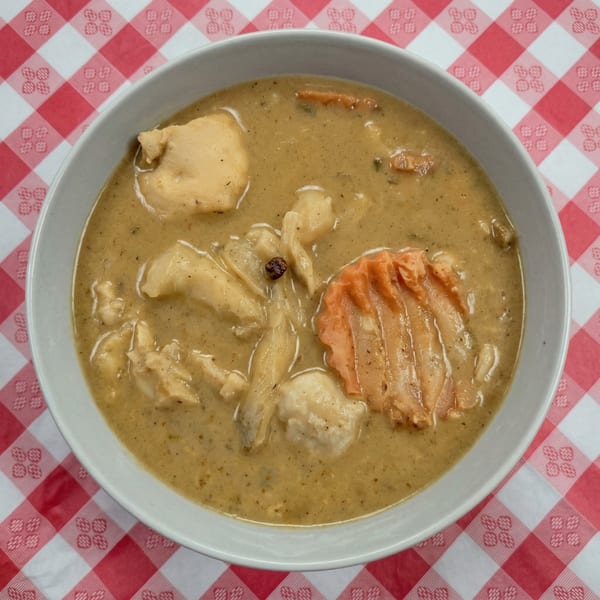 Thai green curry with chicken and vegetables in a white bowl on a red and white checkered tablecloth.