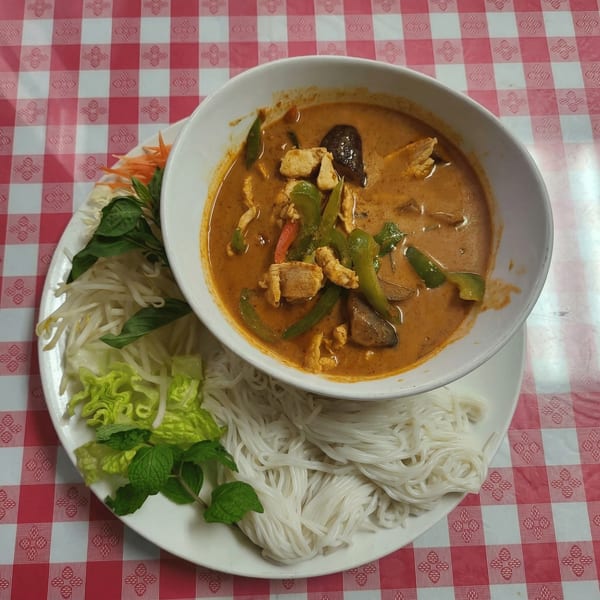 Thai red curry with chicken, bell peppers, and mushrooms, served with rice noodles and fresh herbs.