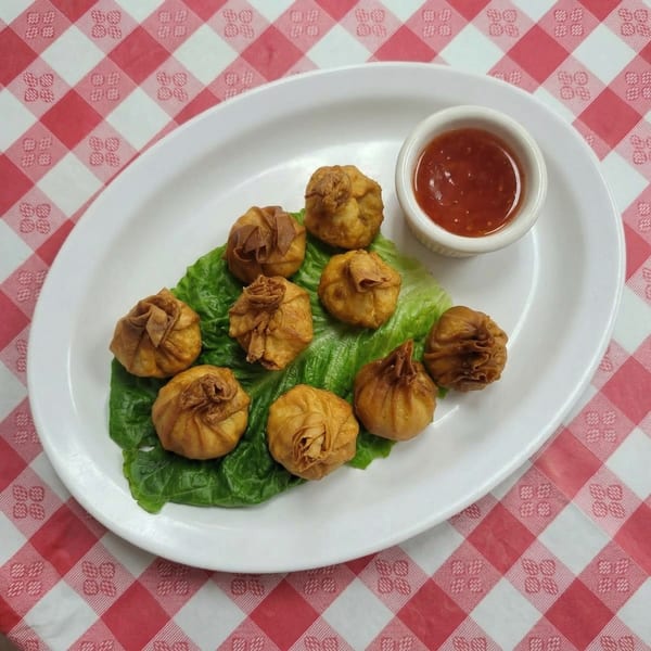 Golden fried Thai dumplings, known as money bags, on lettuce with a side of sweet chili sauce.