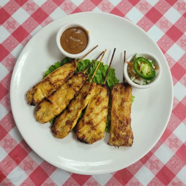 Grilled chicken satay skewers with peanut sauce and a side of pickled vegetables on a white plate.